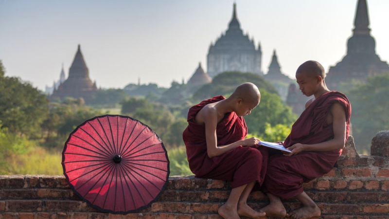Young Monks With The Temple Strewn Skyline Of Bagan In The Background.